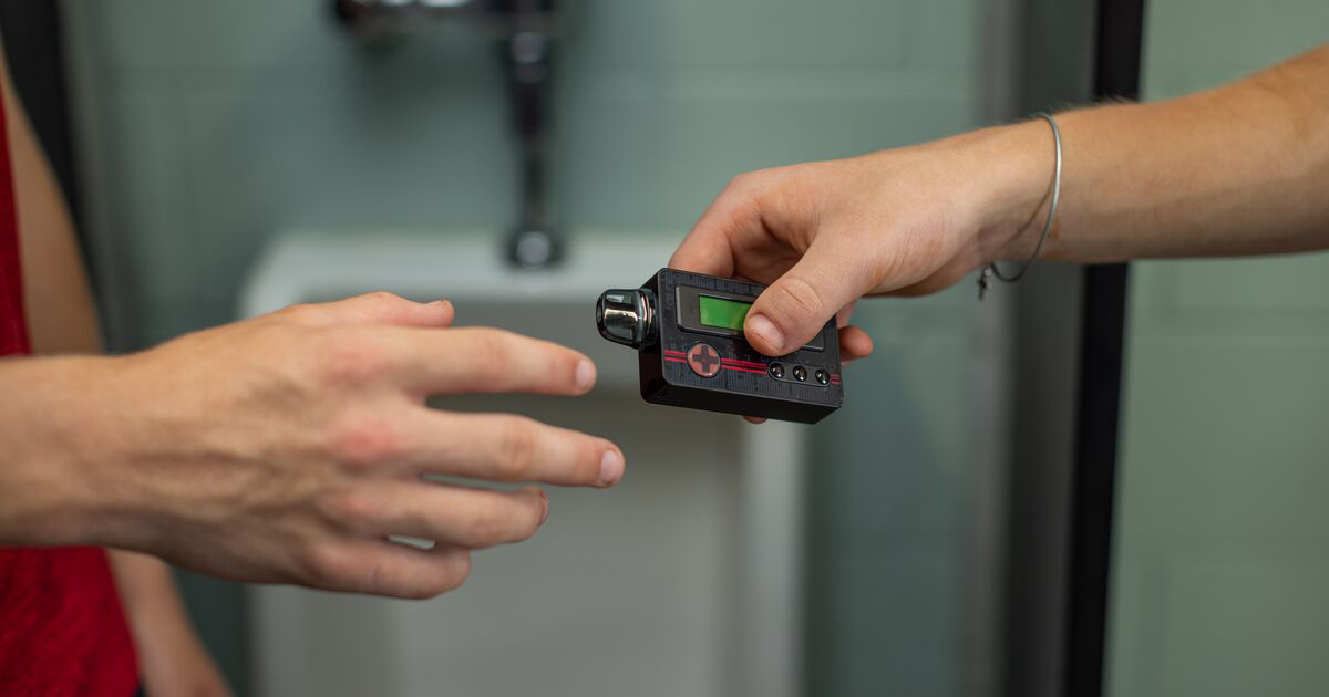 Two students passing a vape that looks like a video game controller in the bathroom