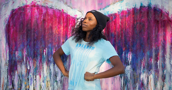 Young, african-american woman standing proudly in front of an urban mural.